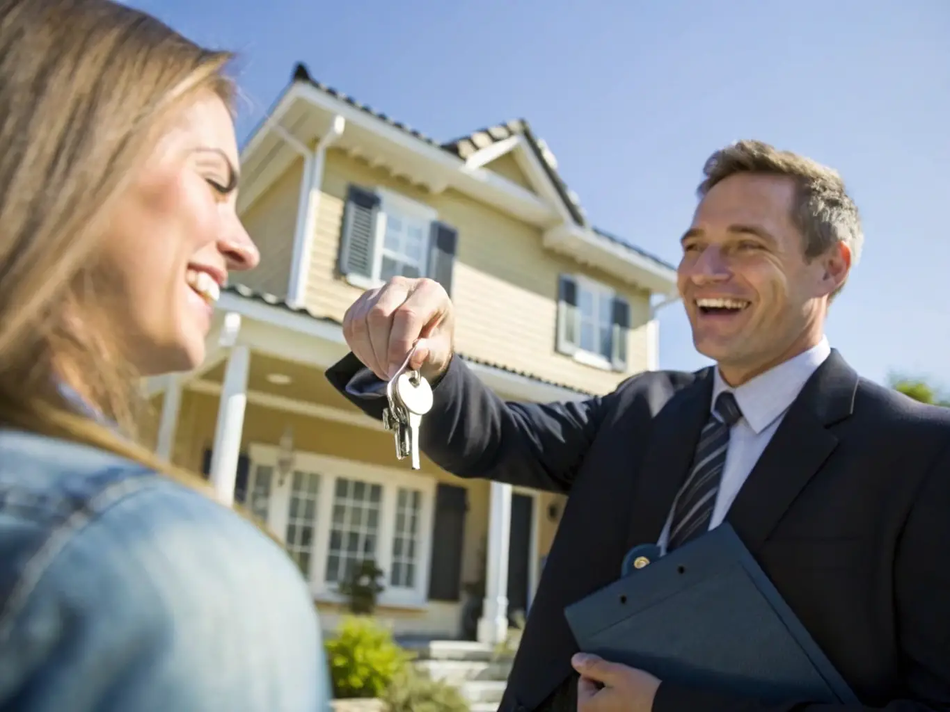 A professional real estate agent handing over keys to a new tenant in front of a well-maintained residential property, symbolizing tenant placement services.